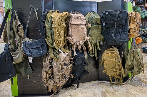US Army Rucksäcke Assault und BW Kampftaschen ich verschiedenen Farben an einen Regal im Outdoorladen