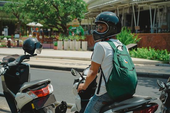 Mann auf Roller mit einen grünen Ticket to the Moon Rucksack auf dem Rücken