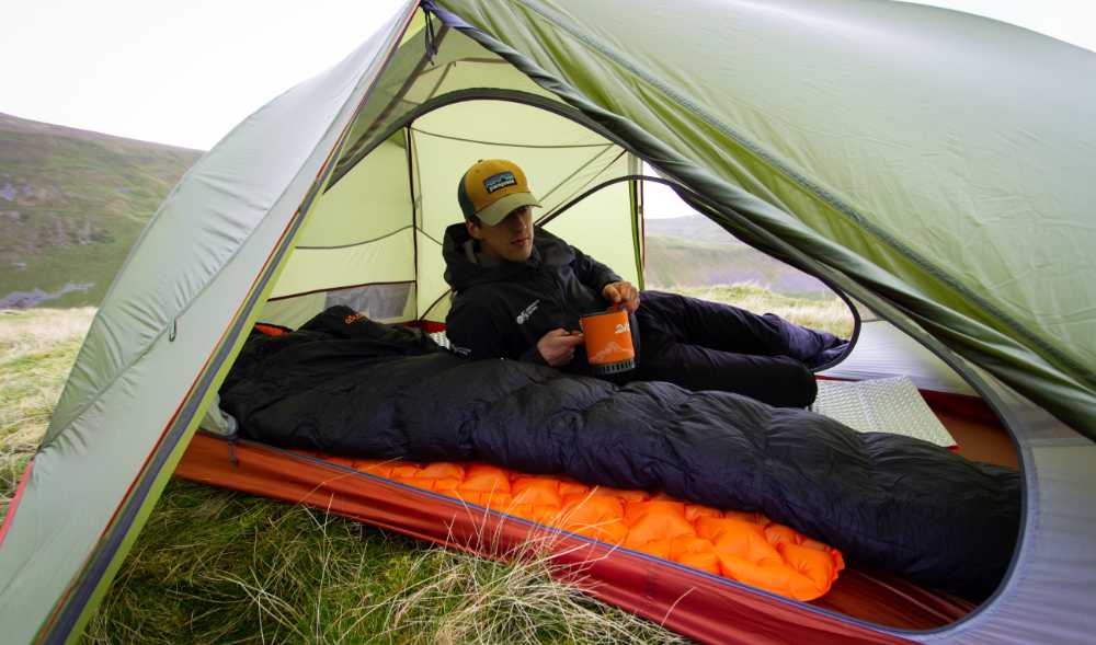 Mann im Trekkingzelt mit Schlafsack und Isomatte.