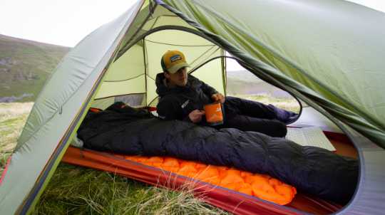 Mann liegt im Trekkingzelt mit einen Schlafsack auf einer Isomatte.