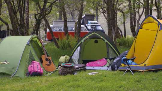 3 Zelte auf einen Festival im halbkreis. In der Mitte liegt eine Gitarre, Rucksäcke und Dreibeine.