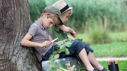 Kinder mit Opinel Kindermesser bei Schnitzen unter einen Baum.