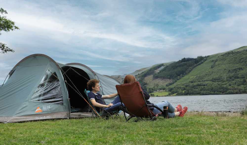 Campingzelt am Fluss mit zwei Personen auf Strandstühlen