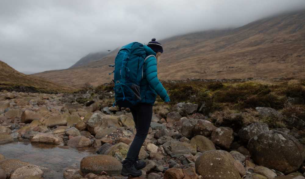 Frau mit Rucksack beim überqueren eines Flusses